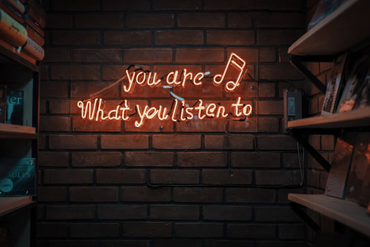 led light sign stating you are who you listen to on a brick wall